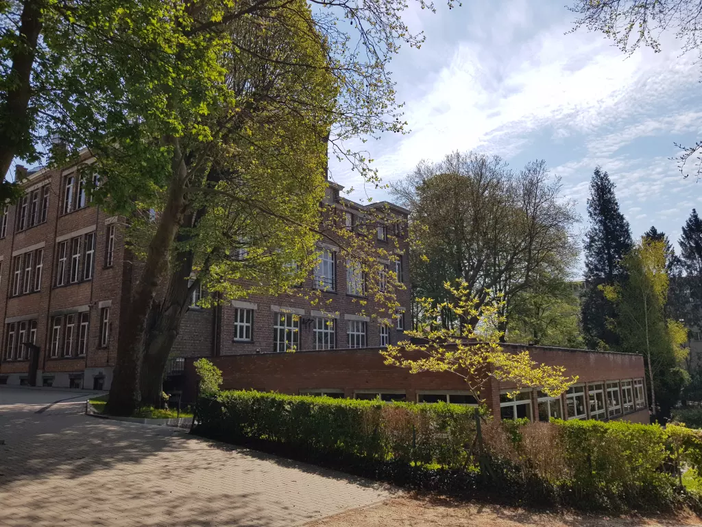 Le bâtiment de briques et ses haies, vus depuis la cour