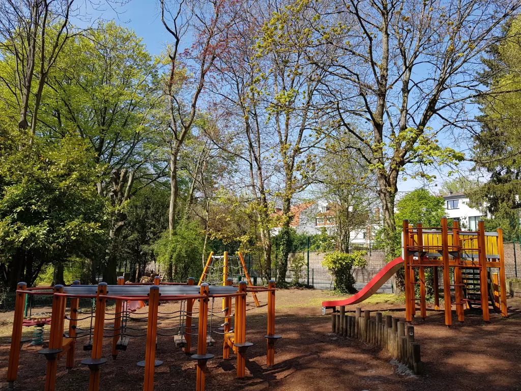 Aire de jeux en bois avec un toboggan rouge, sous les arbres du parc