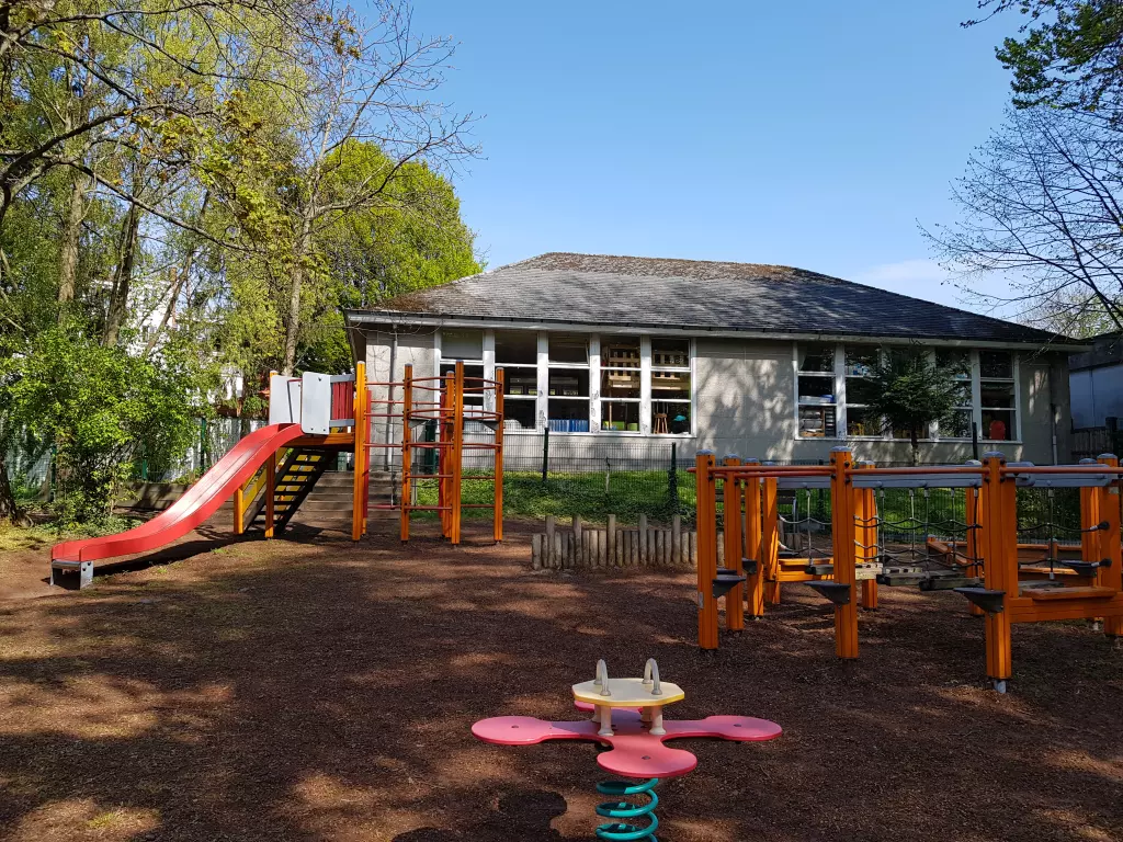 Aire de jeux avec un toboggan et des jeux à ressort devant un pavillon