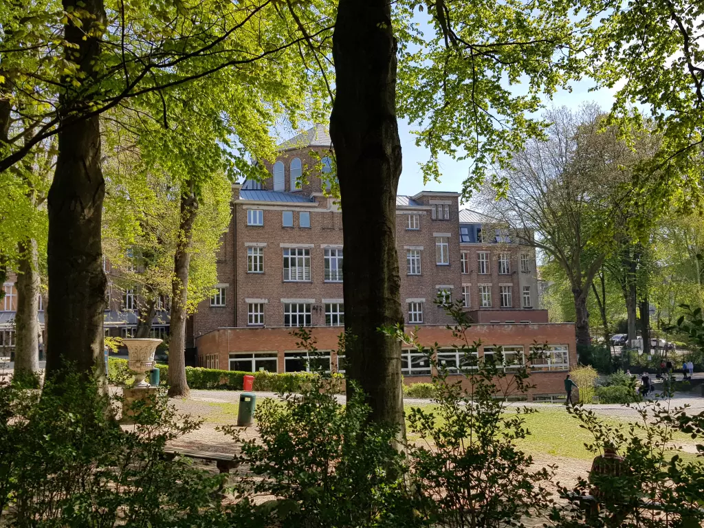 Le bâtiment de l’école vu à travers les grands arbres du parc, au printemps