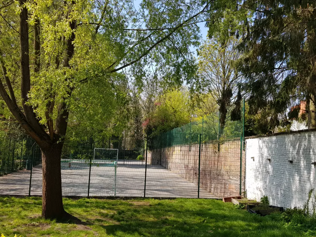 Terrain de sport grillagé derrière une pelouse et des arbres