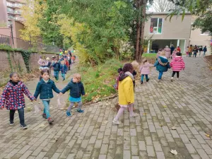 Des enfants de maternelle marchent main dans la main dans l’allée de l’école