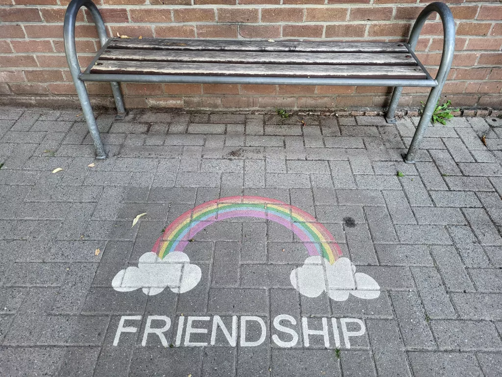 Banc et arc-en-ciel dessiné au sol avec le mot « Friendship »