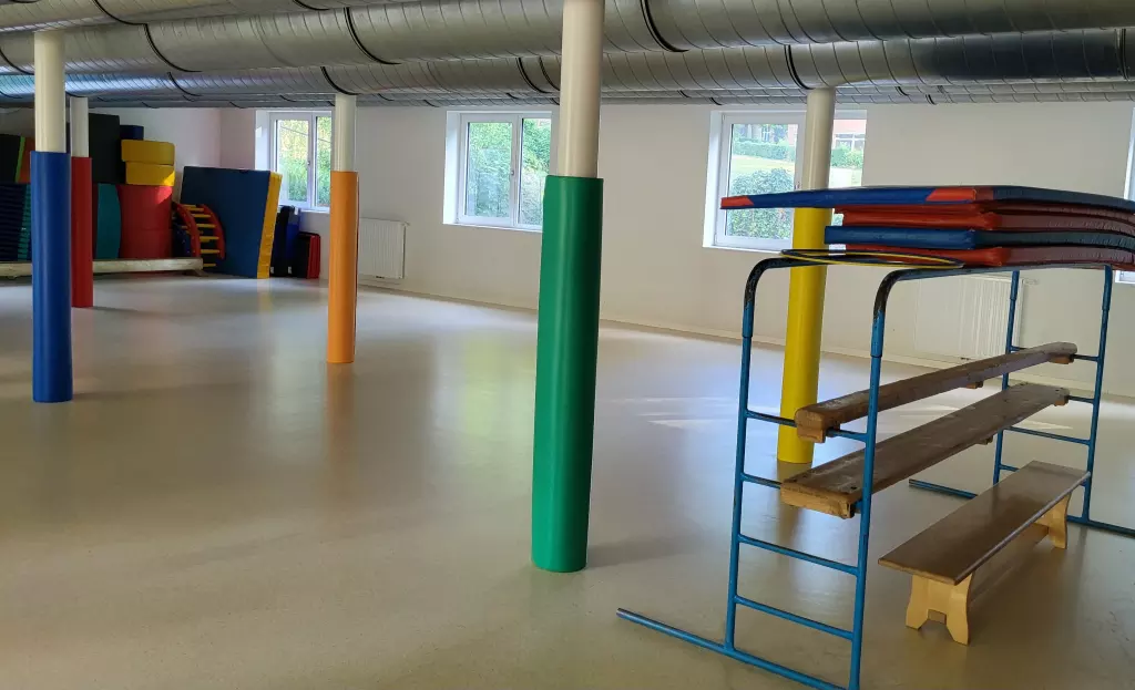 Salle de motricité avec un espalier, un banc et des tapis de couleur
