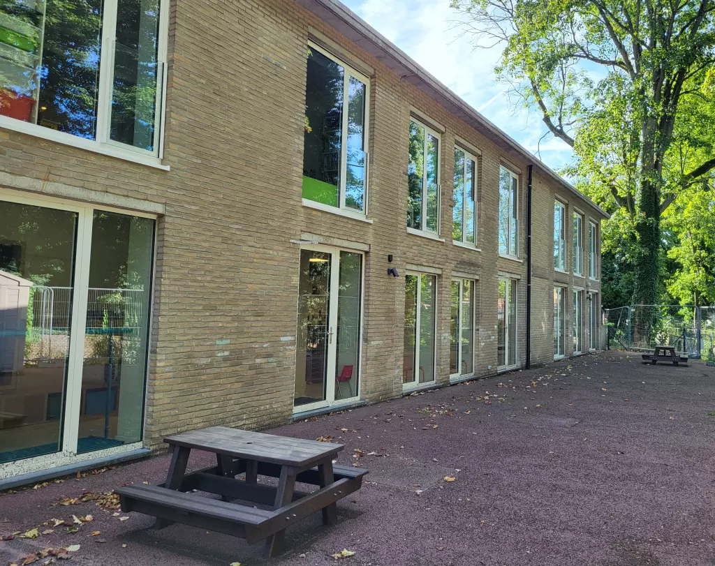 Façade claire d’un pavillon aux grandes baies vitrées, avec une table de pique-nique