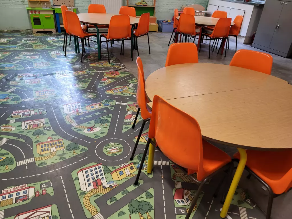 Classe avec des tables rondes, des chaises orange et un tapis de circulation