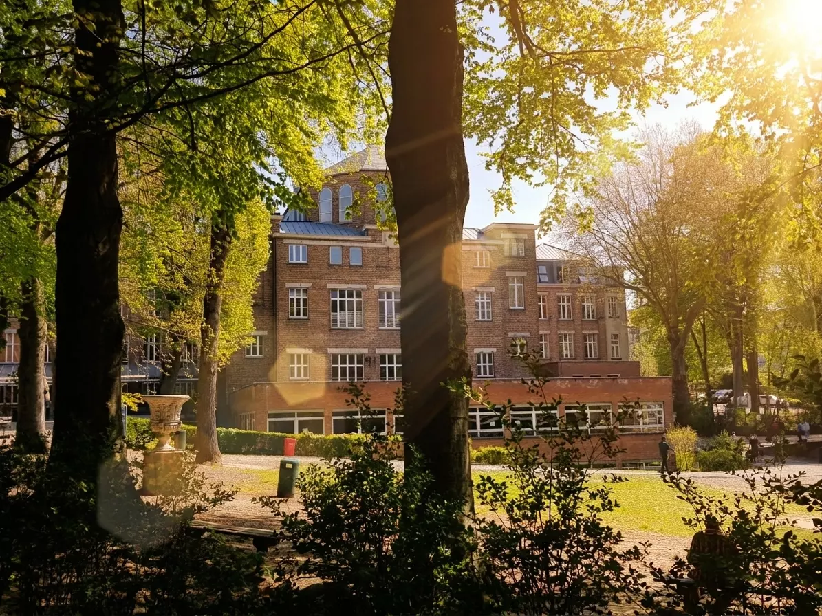 Le bâtiment de l’école vu à travers les grands arbres du parc, au printemps